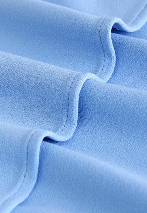 Helles blaues Gewebe mit glatter Textur, das weiche Falten, dezenten Glanz und ordentlich genähte Kanten aufweist. Keine Muster oder Akzente sichtbar.