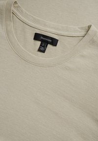 T-shirt beige à col rond fabriqué en tissu doux, présentant une texture ribbed subtile. L'étiquette indique la marque "Matinique" et la taille "L."