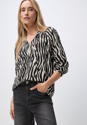 Blouse à rayures zèbres noires et beiges avec des manches longues, un décolleté en V et une coupe décontractée, associée à un jean noir taille haute.