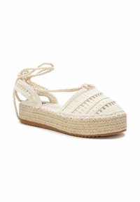 Espadrille de plataforma con parte superior de tela beige trenzada, presenta correas cruzadas y una suela de yute trenzado. Diseño texturizado y ligero.