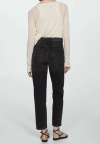 Czarne jeansy z wysokim stanem w dopasowanym kroju, z tylnymi kieszeniami i widocznym przeszyciem, w połączeniu z lekką, przezroczystą bluzką z długim rękawem.