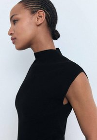 Haut noir sans manches avec un col montant ; texture côtelée ; design ajusté mettant en valeur la silhouette ; style minimaliste et contemporain.