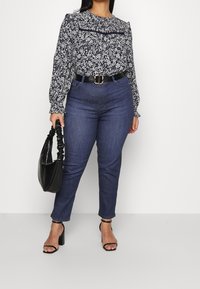 Blusa a manica lunga floreale blu navy con spalle arricciate, abbinata a jeans di denim scuro. Accessoriata con una borsa nera e sandali con cinturini.