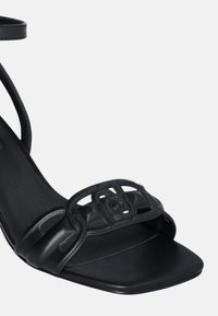 Sandal in pelle nera con punta quadrata, cintura singola e dettaglio decorativo con intagli sulla parte anteriore. Cinturino alla caviglia per una vestibilità sicura.