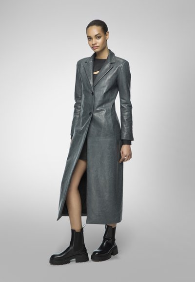 Long, gray leather coat with a notched collar, front buttons, and side slit. Worn with a black mini dress and chunky black ankle boots.