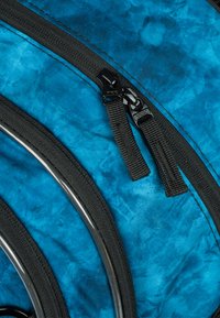 Material della mochilas blu con un motivo tie-dye; presenta cerniere e dettagli neri. Sottolineatura curva bianca evidente lungo i bordi.