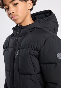 Black padded jacket featuring a zippered front, adjustable hood, and side pockets. Includes a logo patch on the left sleeve. Smooth texture.