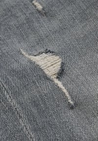 Vervage blauwe denim met versleten patches. Opvallende rafelranden en een gestructureerd weefpatroon, dat de versleten uitstraling van de stof benadrukt.