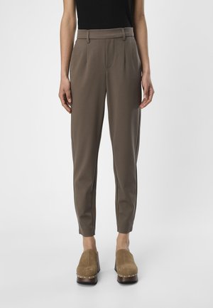 Pantaloni marroni su misura con una texture liscia, caratterizzati da pieghe frontali e un fit affusolato. Abbinati a zoccoli marroni con dettagli borchiati.