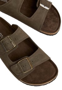 Sandali in suede marrone con due ritagli rettangolari, fibbie metalliche regolabili e un'intersuola texturizzata di colore marrone scuro. Suola in gomma per la presa.