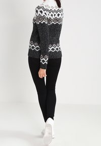 Maglione a maglia con motivo Fair Isle in nero, bianco e grigio. Collo a costine e tessuto lavorato. Abbinato a pantaloni neri slim-fit e sneakers bianche.