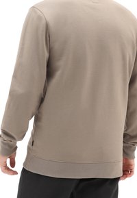 Sudadera de color beige con cuello redondo, mangas largas, puños y dobladillo acanalados, y aberturas laterales. Acabado de tela suave y texturizada.