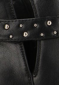 Botín negro de cuero hasta el tobillo con un diseño recortado, acentos de correa con tachuelas y textura suave con detalle de costura en contraste.