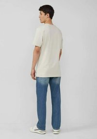 Weißes Baumwoll-T-Shirt mit Rundhalsausschnitt und kurzen Ärmeln, kombiniert mit hellblauen Jeans und weißen Sneakers. Rückansicht dargestellt.