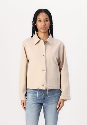 Veste beige à boutons avec un col pointu, des poches frontales et un ourlet à cordon. Manches longues avec une coupe décontractée.