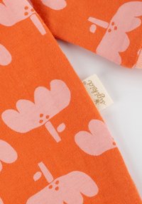 Oranger Stoff mit einem Muster aus rosa Wolken und Bäumen. Strukturierte Baumwolle mit einem kleinen angehängten Etikett.