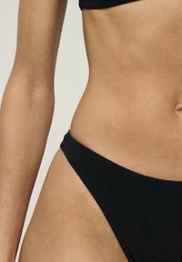 Juodas bikini apatinis trikotažas su lygaus, tampraus audinio, aukštai iškirptomis kojomis ir minimalistiniu dizainu. Nėra matomų raštų ar detalių.