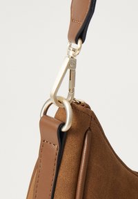 Pruunist seemisnahast käekott, millel on siledast nahast aksendid, kuldse klambri ja kahes toonis rihma disain. Näha on tekstuuriga pinnad.