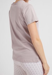 Tílko s krátkým rukávem v jemně fialové barvě z měkké bavlny. Obsahuje kulatý výstřih a pohodlný střih, doplněné bílými legínami s vzorem.