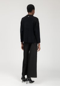 Zwart gebreid sweater met een relaxed fit, verlaagde schouders en een hoge halslijn, gecombineerd met wijdere zwarte broek en puntige enkellaarzen.