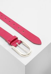Helle pinke Leder-Gürtel mit einer silbernen Metallschnalle. Verfügt über gleichmäßig verteilte Löcher zur Anpassung und hat eine glatte Textur, die zum Ende hin verjüngt.