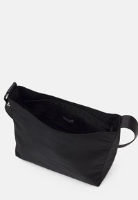 Černá nylonová taška na rameno s hladkou texturou a horním zipem. Má široký otvor, vnější popruh a jednoduchý, minimalistický design.