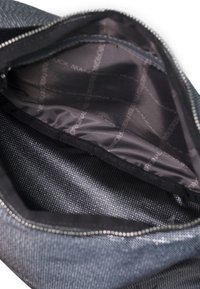 Interno di una borsa in denim scuro con una fodera liscia e lucida caratterizzata da un sottile design a motivi. L'apertura con zip consente l'accesso al compartimento principale.