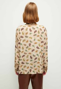 Camisa de manga larga hecha de una tela suave con un fondo beige y un patrón de paisley multicolor. Presenta un corte relajado y puños abotonados.
