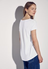 T-shirt bianco a maniche corte con scollatura rotonda e vestibilità morbida. Tessuto liscio; vista posteriore che mostra una leggera curvatura all'orlo.