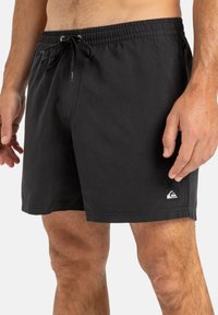 Schwarze Badeshorts aus leichtem Stoff, mit elastischem Bund und Kordelzug, Seitentaschen und einem kleinen Logo am Saum.