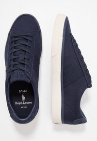 Granatowe płócienne sneakersy z białą gumową podeszwą, z teksturowanymi panelami, okrągłym noskiem, wyraźnym sznurowaniem i markowym logo na języku.