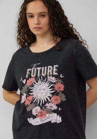 Zwarte katoenen T-shirt met een ronde hals en een bloemenzonneafbeelding in zachtroze, wit en grijs, met de tekst "De toekomst is helder."