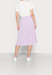 Lichtpaarse midi-jurk met een elastische tailleband, gecombineerd met een wit T-shirt en witte schoenen. Glad stoftextuur.