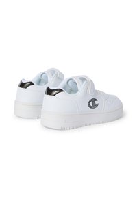 Sneakers bianchi in pelle con una texture liscia, accentuati da un dettaglio nero sul tallone e un logo di strass di lato. Presentano una suola in gomma e una tracolla in Velcro.