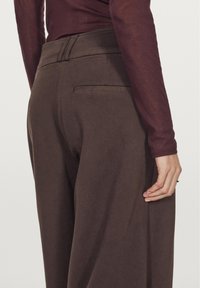 Brązowe szerokie spodnie wykonane z teksturowanej tkaniny, z tylną kieszenią i gładkim pasem, w zestawieniu z dopasowaną bordową bluzką z długim rękawem.