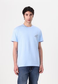 T-shirt en coton bleu clair avec des manches courtes, un col rond et un petit imprimé graphique noir sur la poitrine gauche. Coupe décontractée.