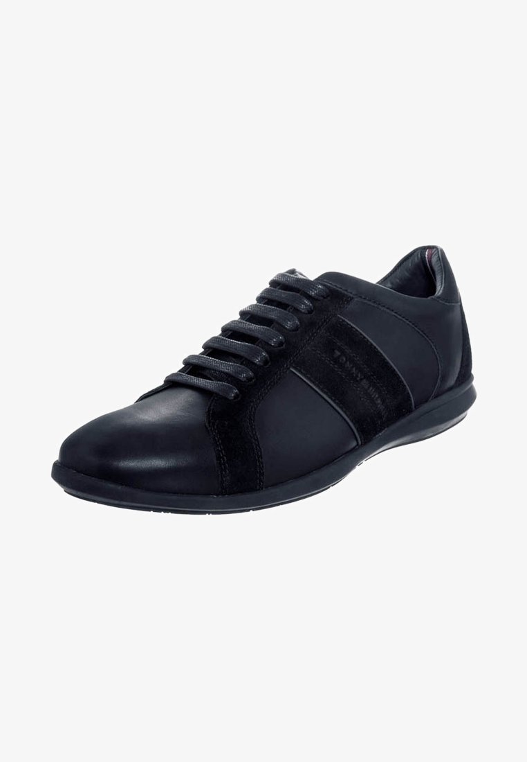 Baskets basses en cuir noir avec lacets noirs et panneaux latéraux en daim, présentées légèrement en angle sur fond blanc.
