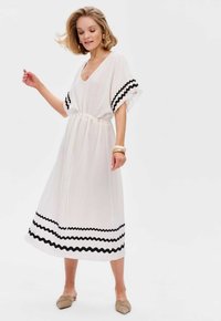 Witte jurk met een V-hals, korte brede mouwen en een verstelbare koord in de taille. Zwart golvend patroon langs de zoom. Zacht, lichtgewicht materiaal.
