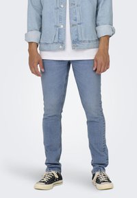 Lys blå denimjakke og tettsittende lys blå jeans, brukt sammen med en hvit t-skjorte og svarte joggesko. Detaljer inkluderer metallknapper og sømmer.