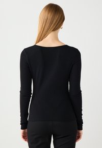 Schwarzes Langarmoberteil mit geripptem Design und rundem Rückenausschnitt. Figurbetonte Silhouette bis zur Taille, kombiniert mit schwarzen Hosen.