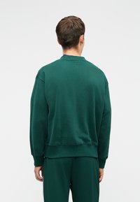 Felpa verde in cotone con scollo rotondo, spalle scese e polsini a costine. Texture liscia con una silhouette morbida e comoda.