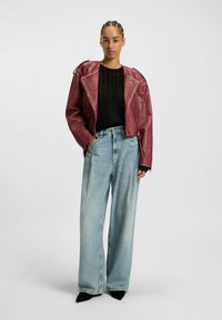 Veste de moto en cuir bordeaux avec des accessoires en métal argenté, haut noir texturé et pantalon en denim large bleu clair. Chaussures noires à bout pointu.