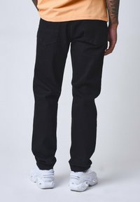 Vaqueros de mezclilla negra con piernas rectas, que cuentan con dos bolsillos traseros y costuras visibles. Se llevan con zapatillas blancas y una camisa naranja.