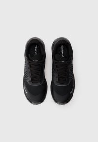 Une paire de baskets noires avec des lacets, des accents en lignes courbes blanches et une marque visible, vues de dessus sur un fond clair uni.