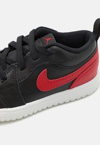 Sorte lædersneakers med røde detaljer, der har et rødt logo, sorte snørebånd, en polstret krave og en hvid sål med struktureret greb.