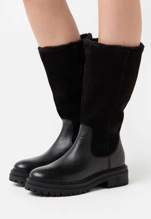 Zwarte kniehoge laarzen met een combinatie van glad leer en zachte suède. Dikke, gestructureerde rubberen zool met een laag hakje.