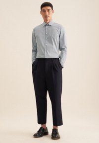 Camicia a quadri bianco e azzurro chiaro con bottoni, pantaloni neri a vestibilità rilassata e scarpe nere. Tessuto morbido con un design strutturato.