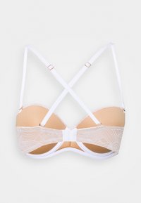 White lace bra with padded beige cups and adjustable crisscross straps on a plain background.