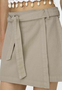 Beiger Wickelrock aus strapazierfähigem Stoff, mit seitlicher Bindegürtel und sauberem Saumabschluss. Minimalistisches Design ohne Muster.