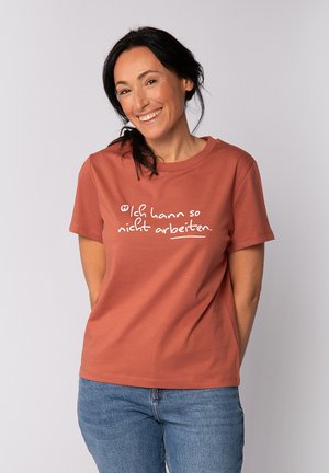 Rust-colored T-shirt made of cotton, featuring white text that reads "Ich kann so nicht arbeiten." Short sleeves and a crew neckline.